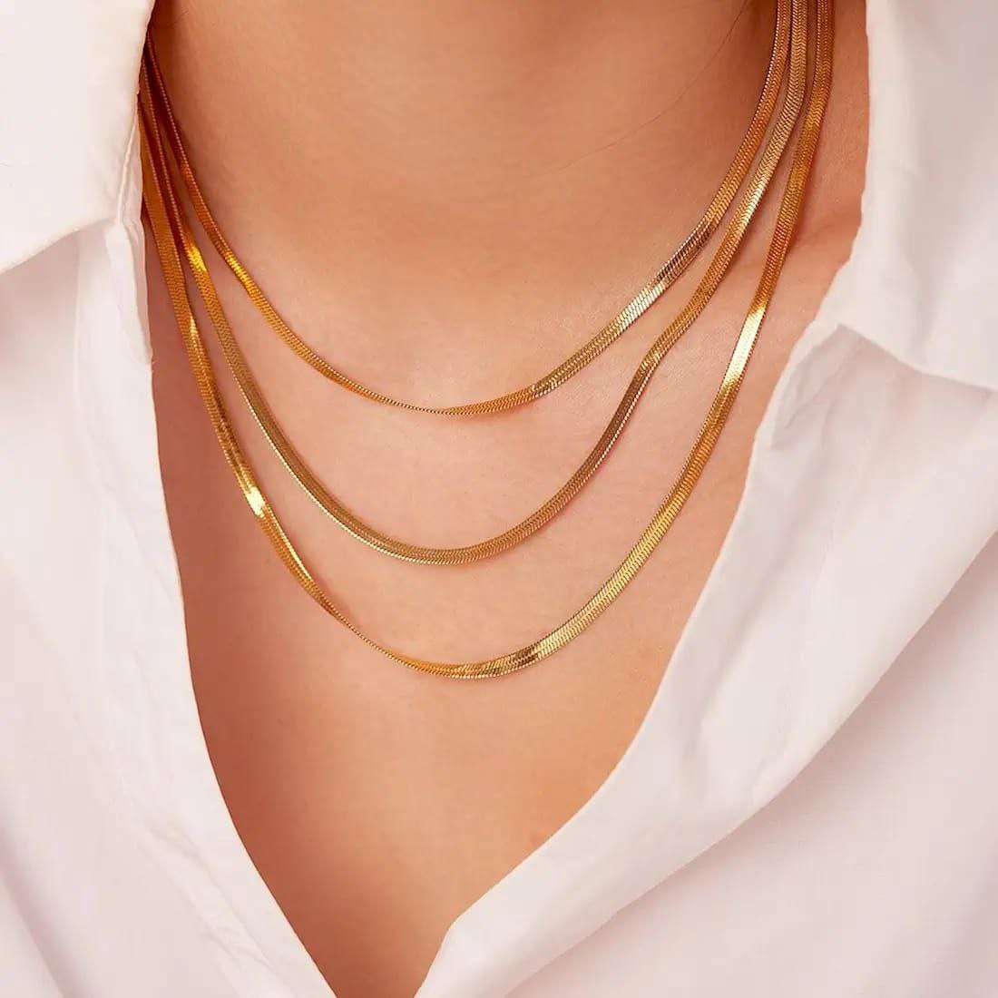 Three gold necklaces on a person wearing a white shirt