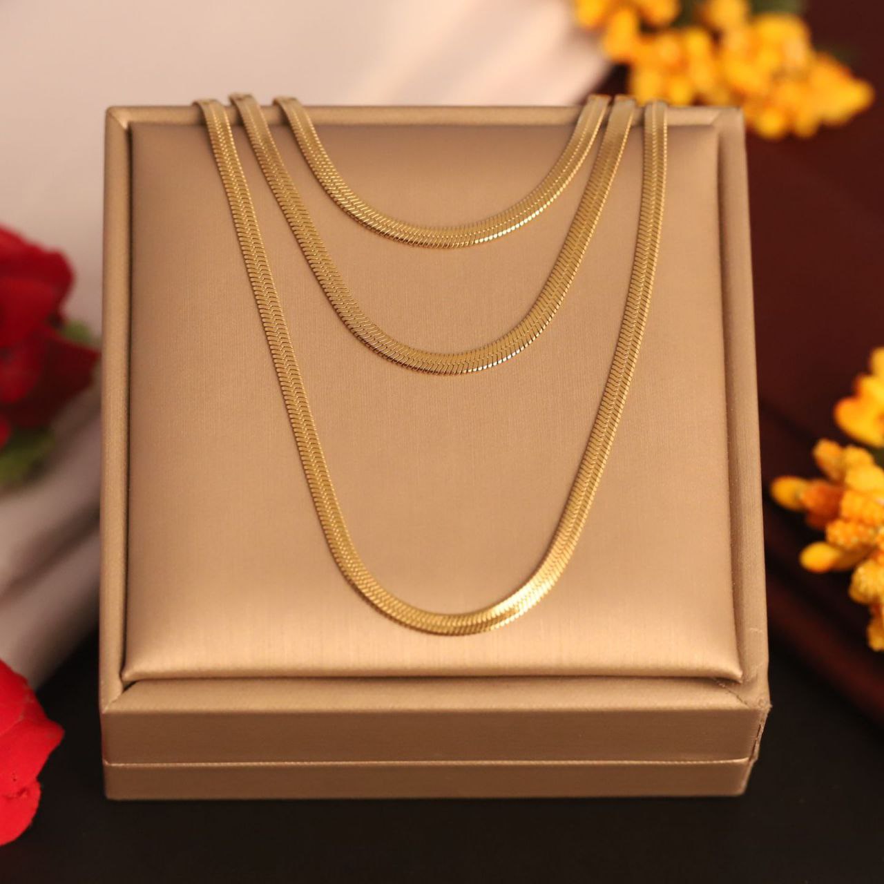 Gold necklace on a beige jewelry box with flowers in the background