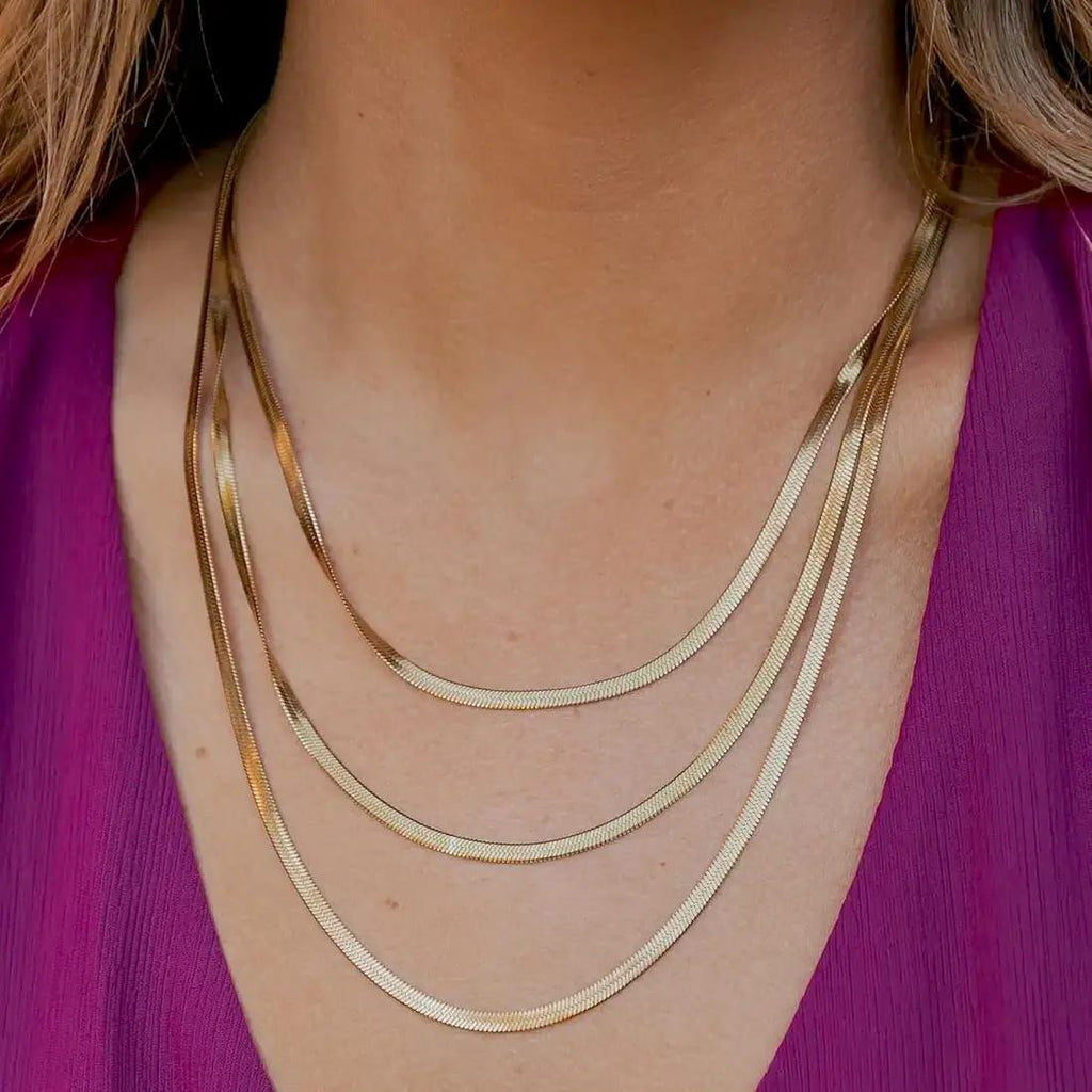 Close-up of a person wearing a gold necklace against a purple garment.