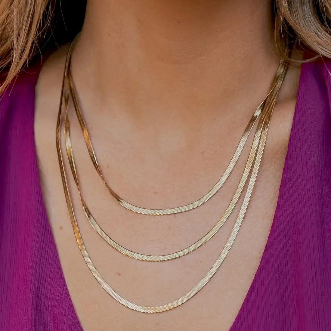 Close-up of a person wearing a gold necklace against a purple garment.